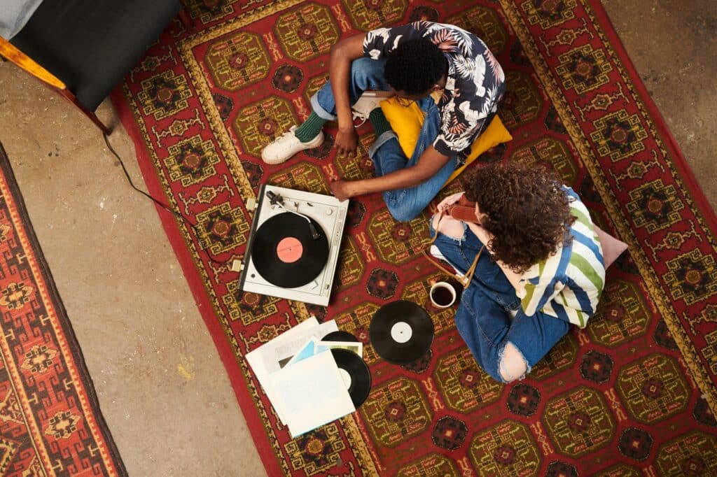 Above angle of two zoomers in stylish casualwear listening to vynil disks